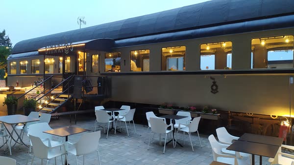La carrozza vista di lato all'imbrunire, i finestrini accesi e i tavolini del dehors davanti