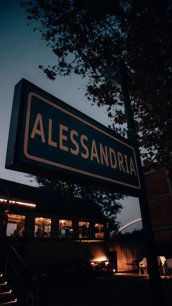 Il cartello ferroviario ALESSANDRIA davanti al locale, con la carrozza illuminata sullo sfondo