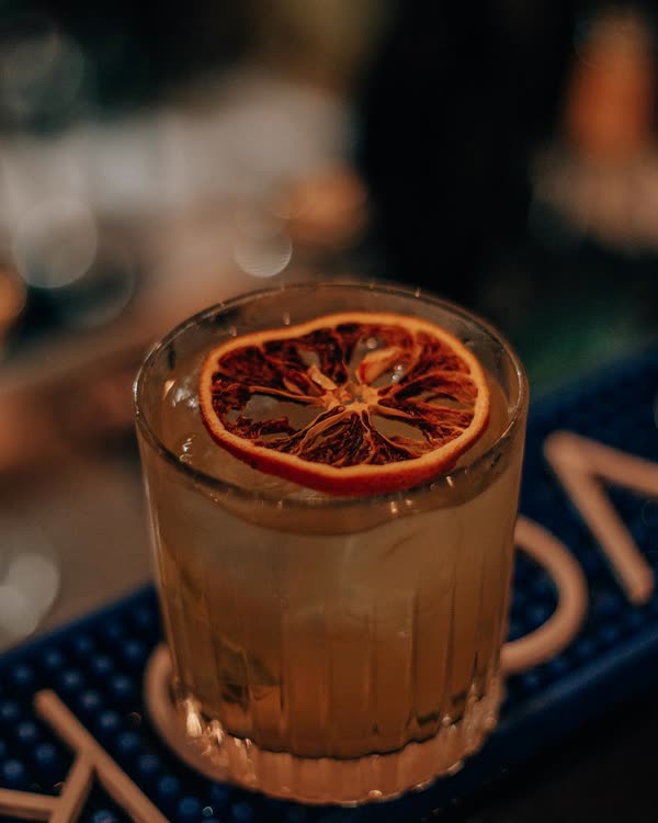 Un cocktail servito con una fetta di arancia disidratata sul bancone del bar