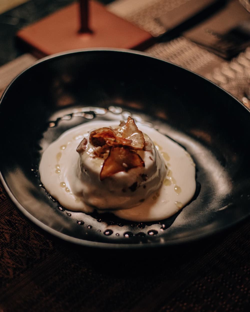 Flan di topinambur con crema di castelmagno, castagne e cioccolato bianco, servito in una ciotola nera sotto la luce calda del vagone